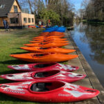 Club whitewater kayaks laid out on the bank of the River Wey in front of the club building